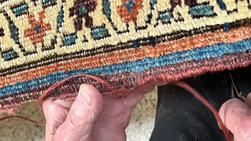 Hands working fringe repair on a rug
