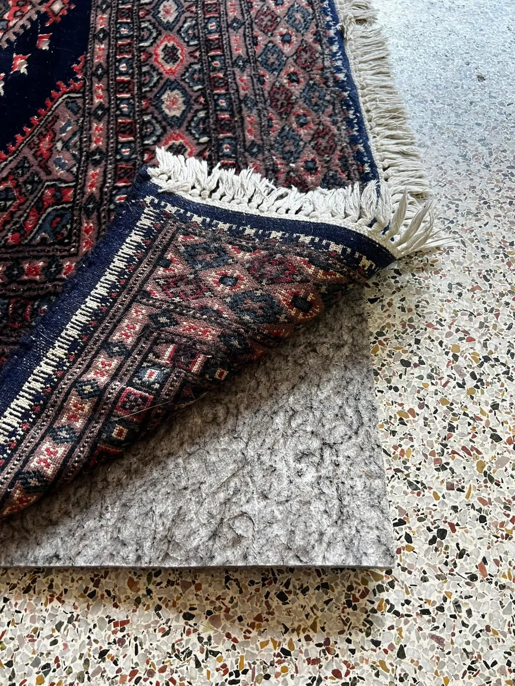 A Bokhara rug corner folded back to show the felt rug pad beneath